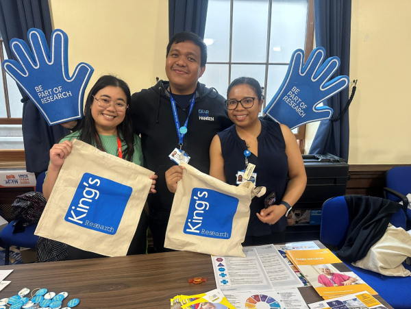 Three members of the NIHR King's Clinical Research Facility team standing in front of a stall for International Clinical Trials Day